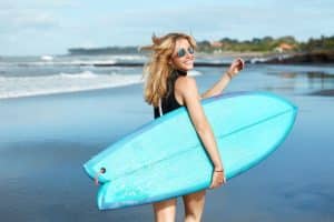 woman holding surfboard at the beach smiling