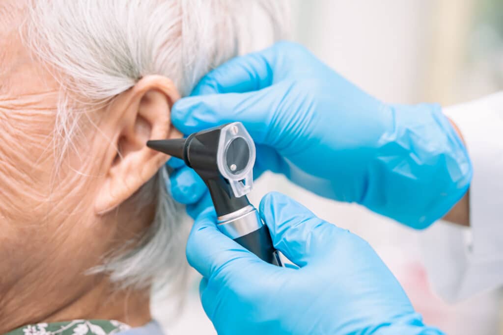 Audiologist or ENT doctor use otoscope checking ear of senior woman patient treating hearing loss problem.